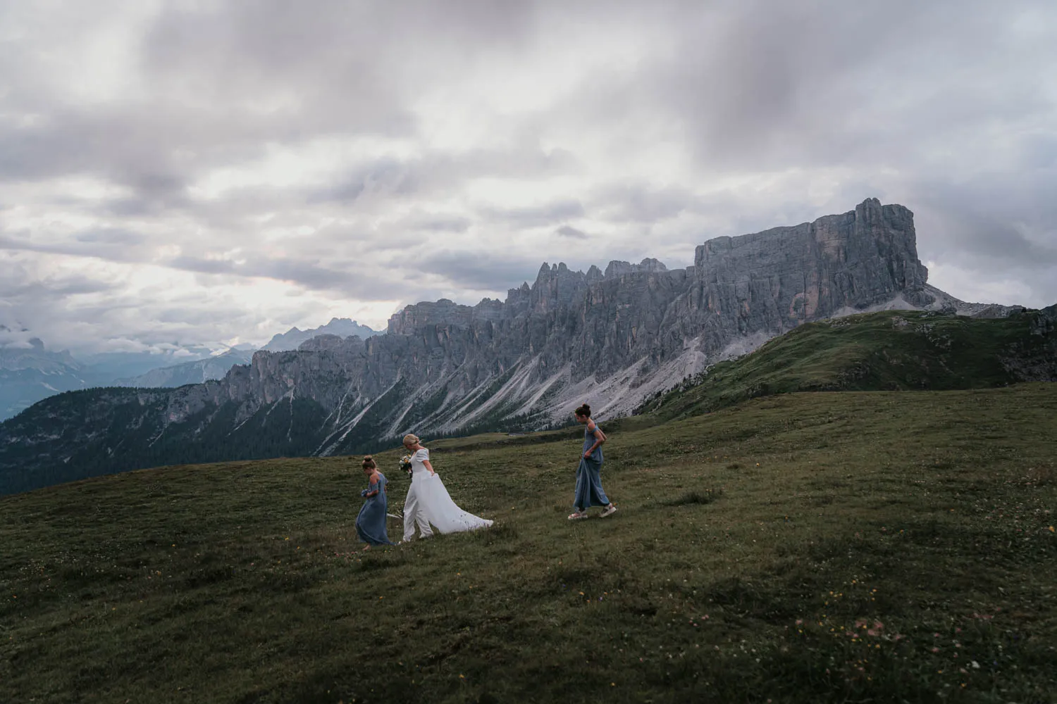 A couple small on a green meadow beneath the Ra Gusela and Croda da Lago peaks
