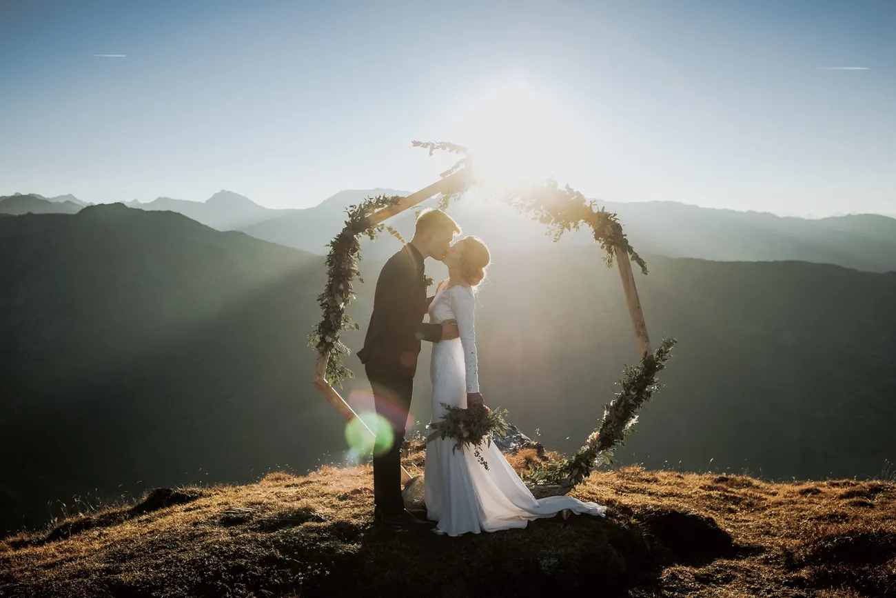 The couple at a floral arch backlit by a blazing Tyrolean sunset
