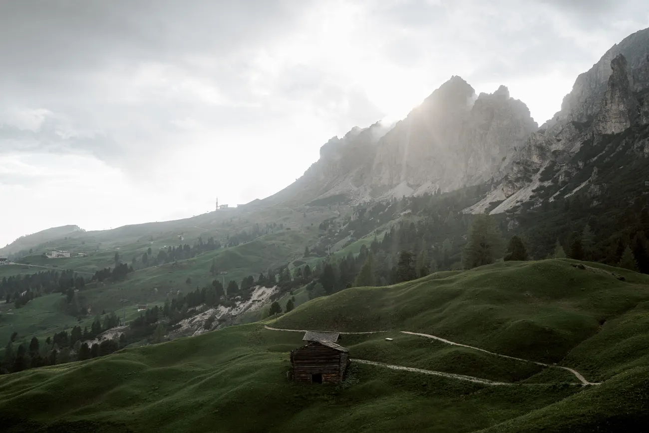 Green meadow and a hut at Passo Gardena as the sun breaks through