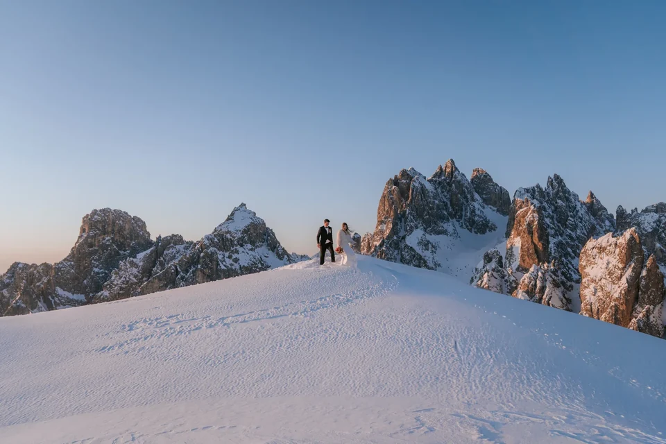 The couple tiny on a snowy ridge beneath the jagged winter peaks
