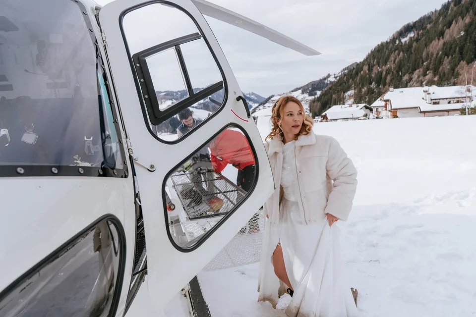 A bride in a winter coat stepping out of the helicopter into the snow