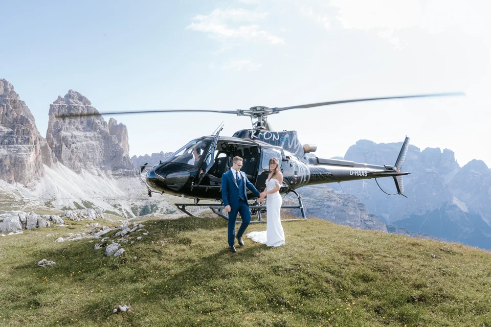 The couple beside the helicopter on a ridge, veil in the wind