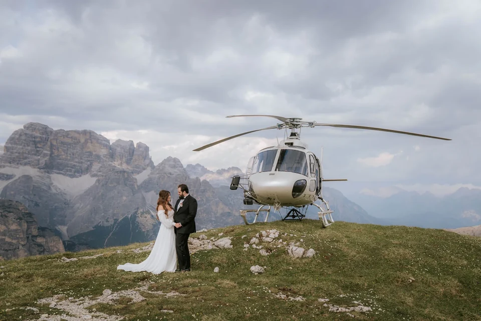 The couple alone on a ridge with the helicopter and a Dolomite panorama