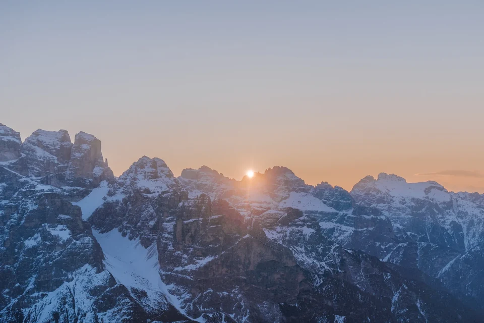 Die Sonne bricht über schneebestäubten Dolomitengipfeln hervor